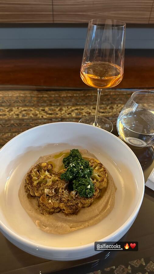 A grain bowl with greens and a glass of wine