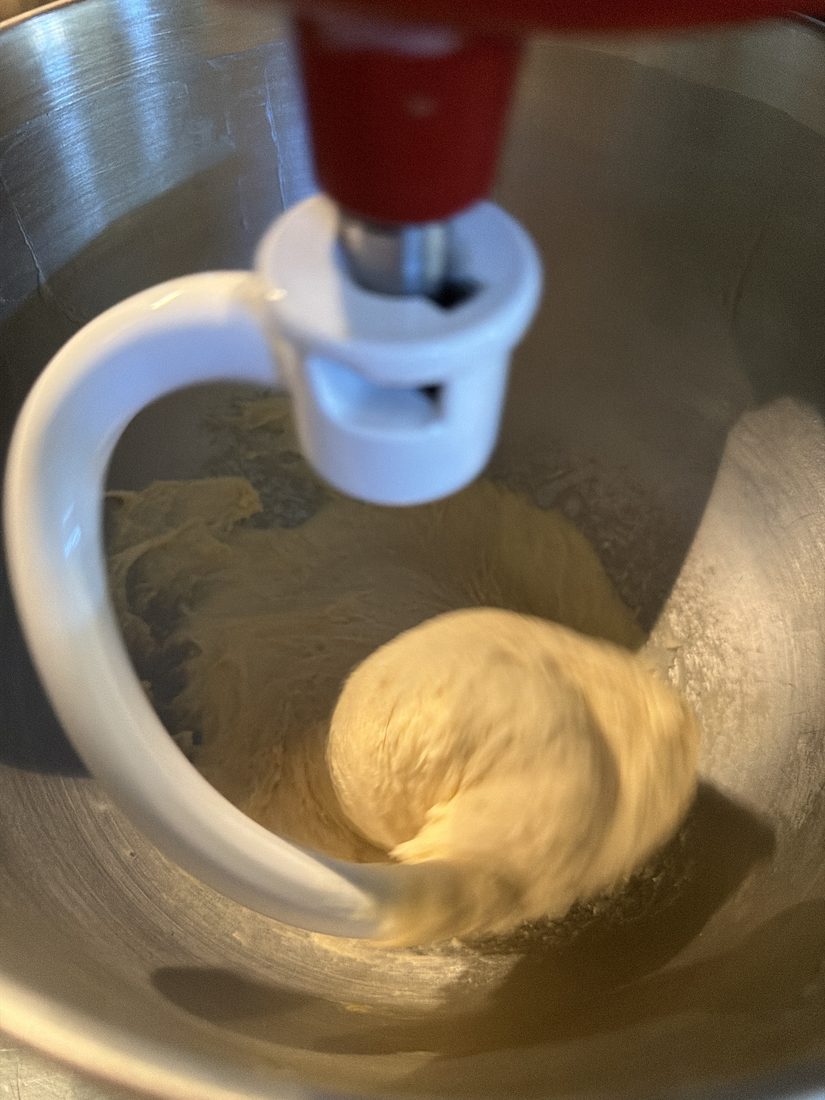 Enriched dough kneading on the dough hook of a stand mixer, smooth and pale.