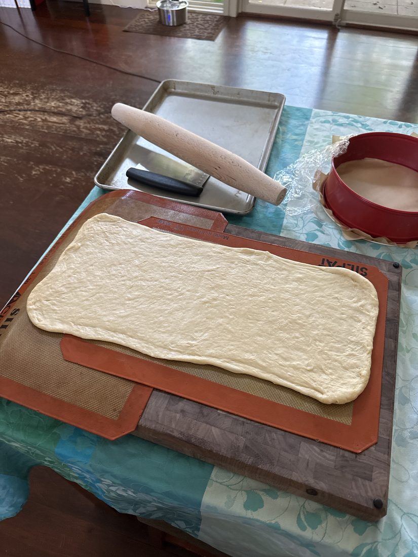 A sheet of dough rolled out on the counter next to a rolling pin, bench scraper and the lined springform pan.