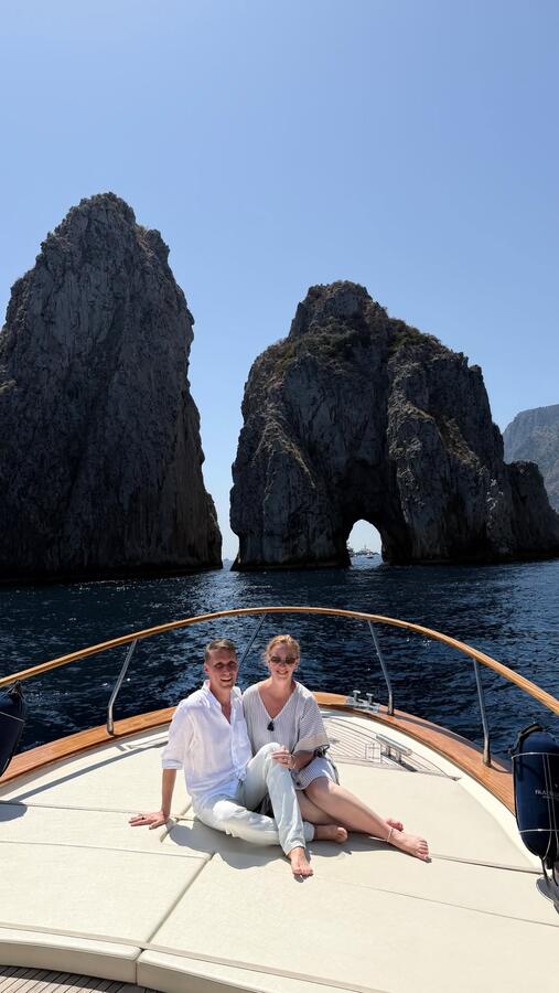 Two people on the bow of a boat below the Faraglioni rocks off Capri