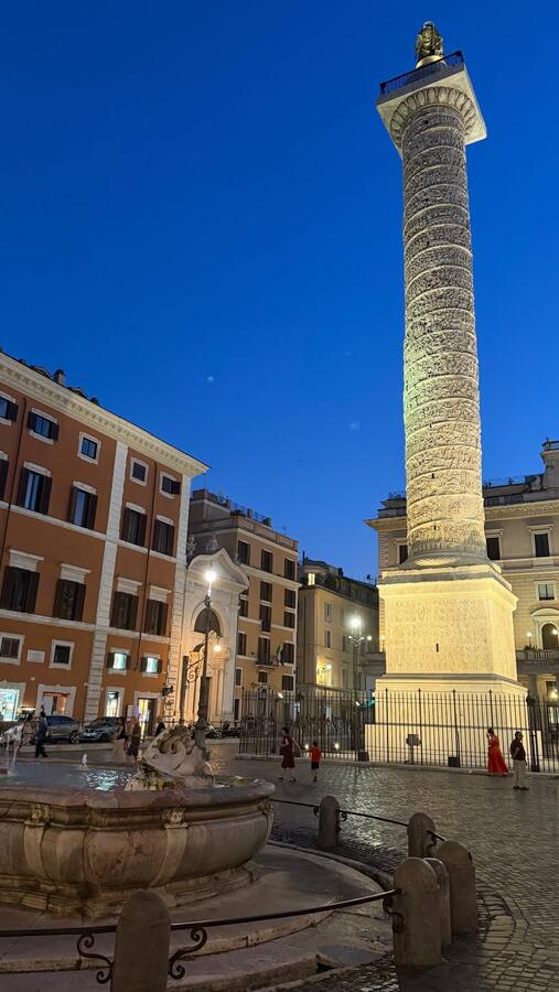 A Roman column lit at night above the ruins